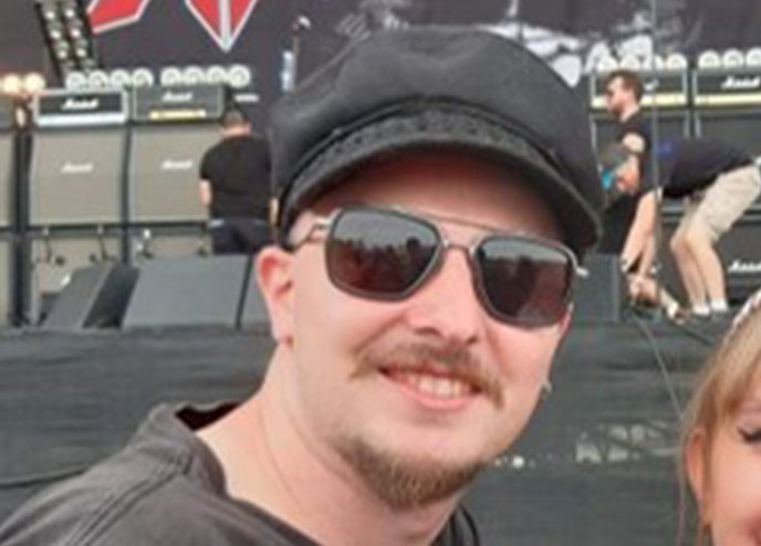 Care Workforce Assistant Nathan Coombes smiling at the camera in a black cap and sunglasses, at a festival concert.