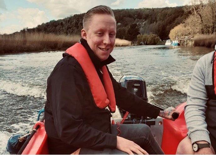 Communications & Engagement officer Danny driving a small red boat on the river Arun, while smiling at the camera.